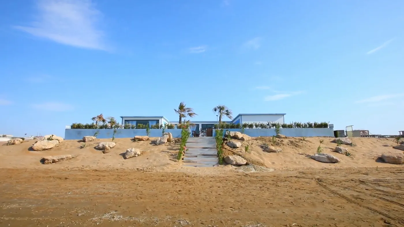 The restaurant from the beach: a white pavilion beyond sand and rocks